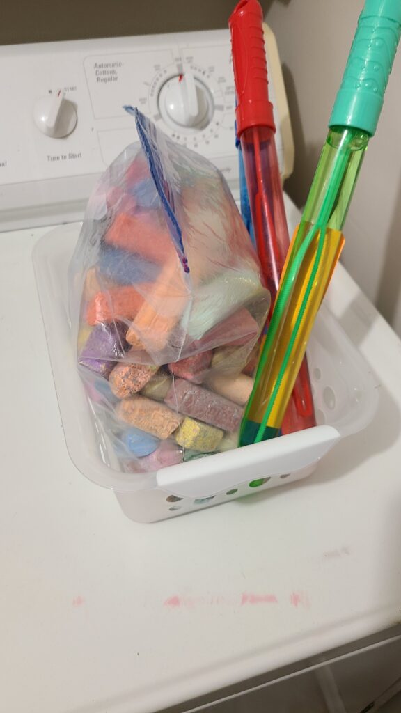 A small organizing bin filled with a bag of chalk and bubble wands.