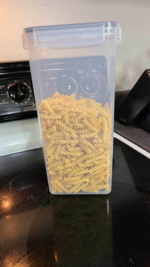 A clear food container filled with rotini pasta