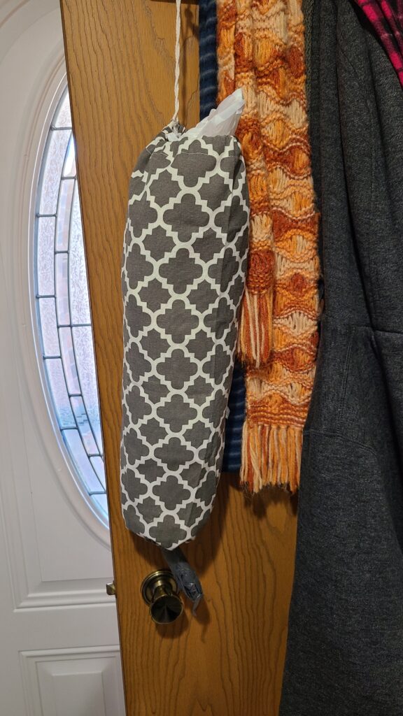 The inside of a closet door. Hanging on a hook is a bag holder made of cloth.