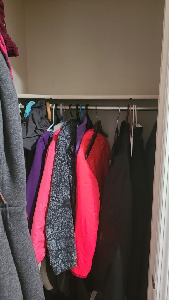 The inside of a front closet. It has been cleaned out and a few coats are hung up inside.
