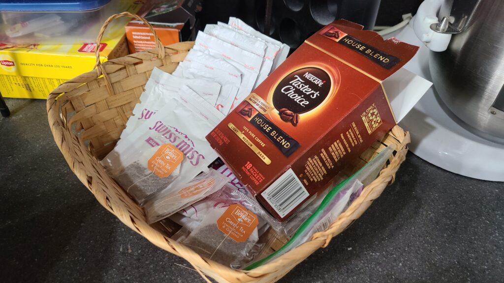 A small wicker basket filled with hot chocolate packets, tea bags, and coffee packets