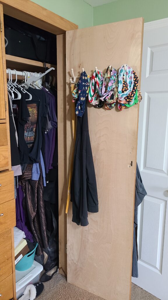 An open closet door. On the inside of the door is a set of wall hooks, with headbands hanging on them.
