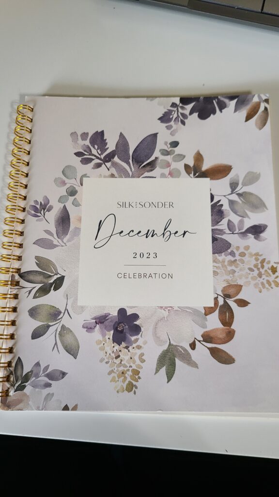 A small planner on a desk top. The cover says "Silk and Sonder, December 2023"