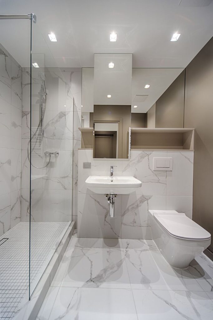A bathroom. To the left is a walk-in shower, in the middle is a small sink, and on the right is a toilet.