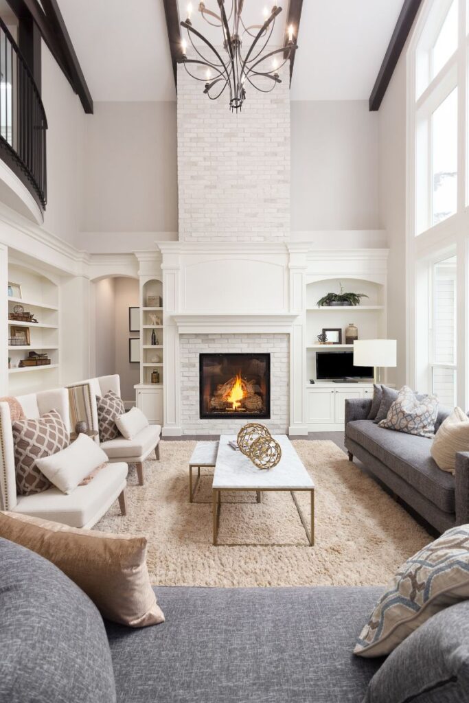 A bright living room with a couch and two chairs. In the background is a lit fireplace.