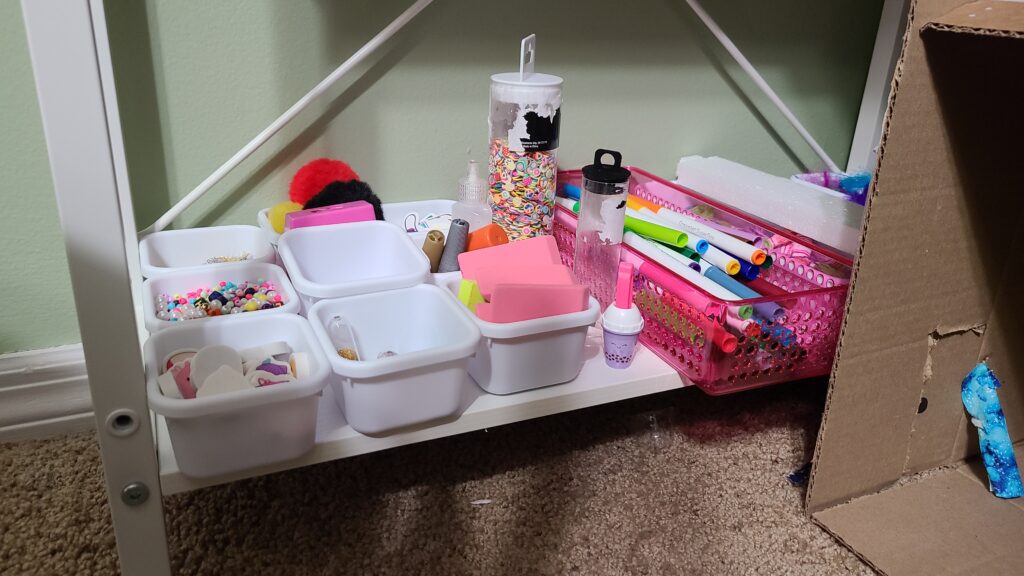A closeup of a shelf under a desk. On the shelf are drawer dividers filled with craft supplies.