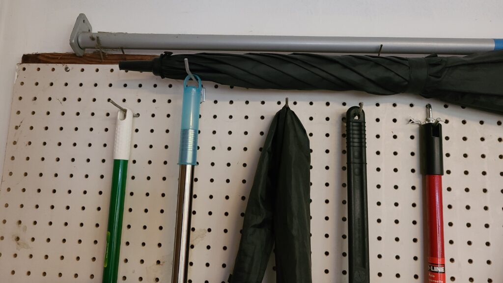 A large pegboard on a garage wall, with hanging brooms and mops