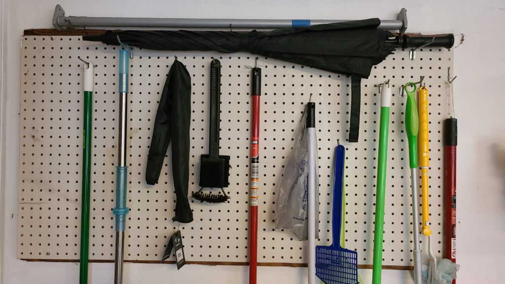 A large pegboard on a garage wall, with hanging brooms and mops