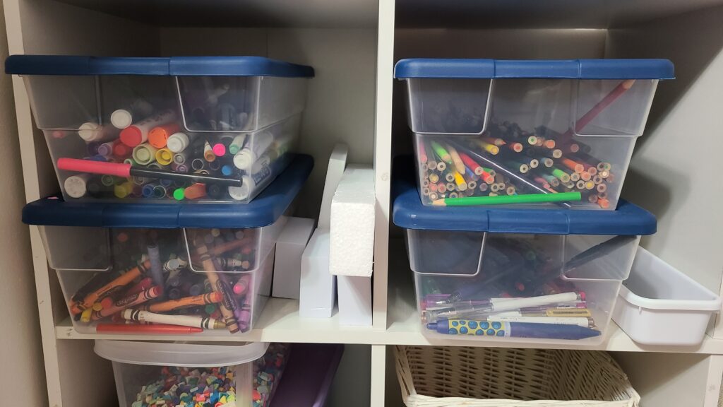 A closeup of a cube shelf. In two of the cubes are storage bins filled with art supplies.