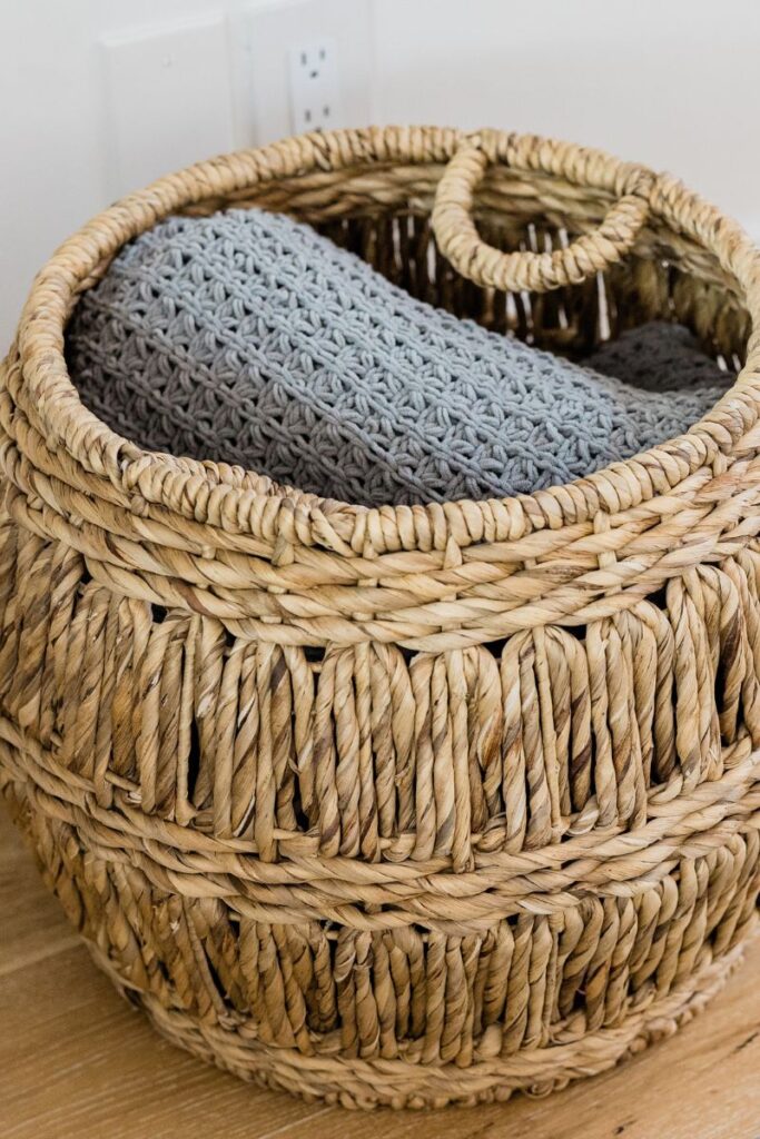 A circular wicker basket filled with a crocheted blanket