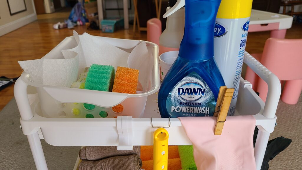 The top shelf of a rolling cart, containing cleaning sprays and sponges.