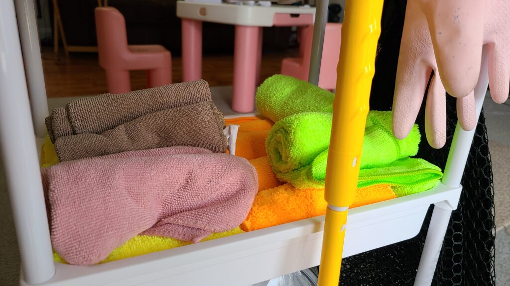 The middle shelf of a rolling cart, filled with rolled-up microfiber cloths.