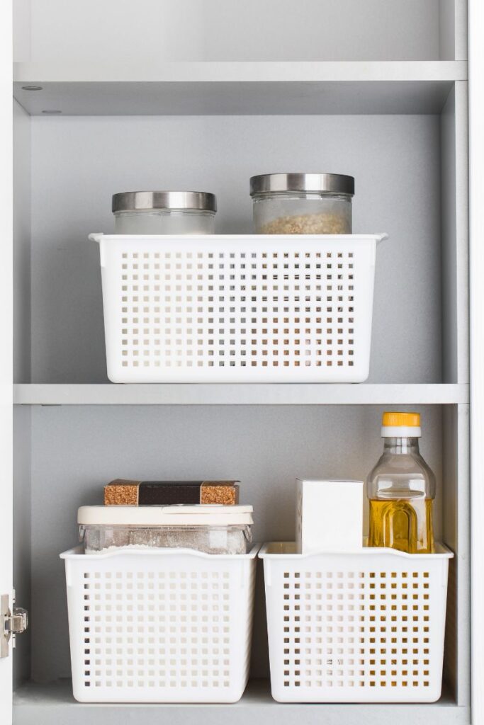 The inside of a cabinet. On the shelves are jars sitting inside small baskets.
