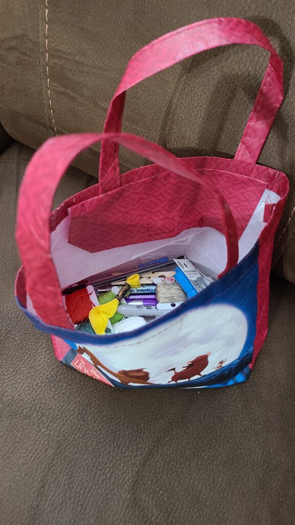 A small bag with handles. Inside are cross stitch supplies.