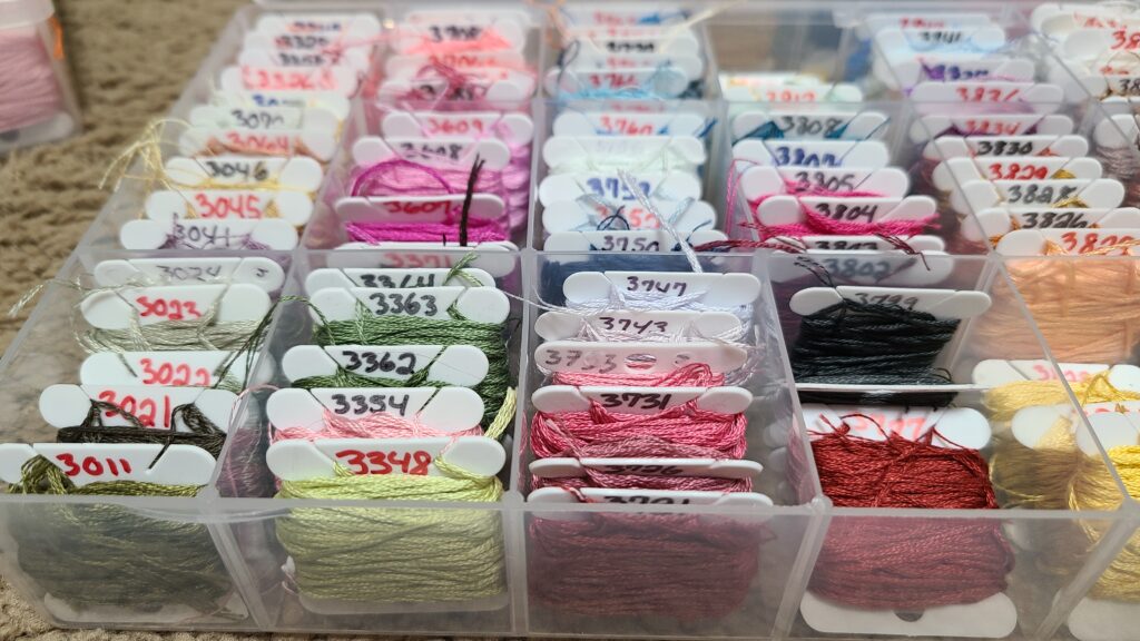 A closeup of a plastic craft organizer. Inside are numbered bobbins with colored floss.