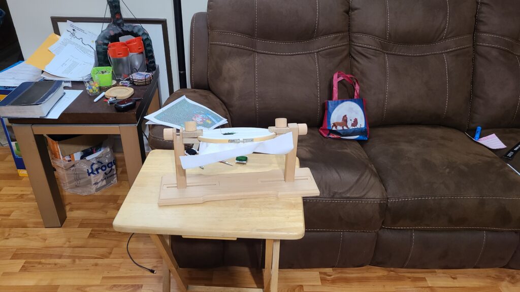 A living room couch. On it are cross stitch supplies.