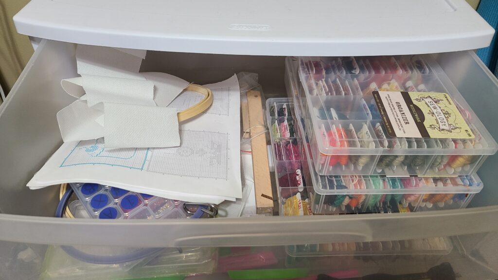Inside of a drawer of a Sterilite cabinet. Inside are plastic craft organizers and other cross stitch supplies.