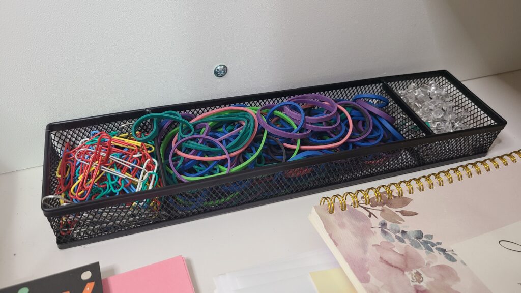 A divided basket filled with paper clips, rubber bands, and pins
