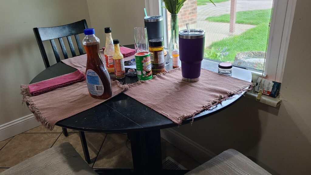 A kitchen table topped with placemats, cups, and condiments