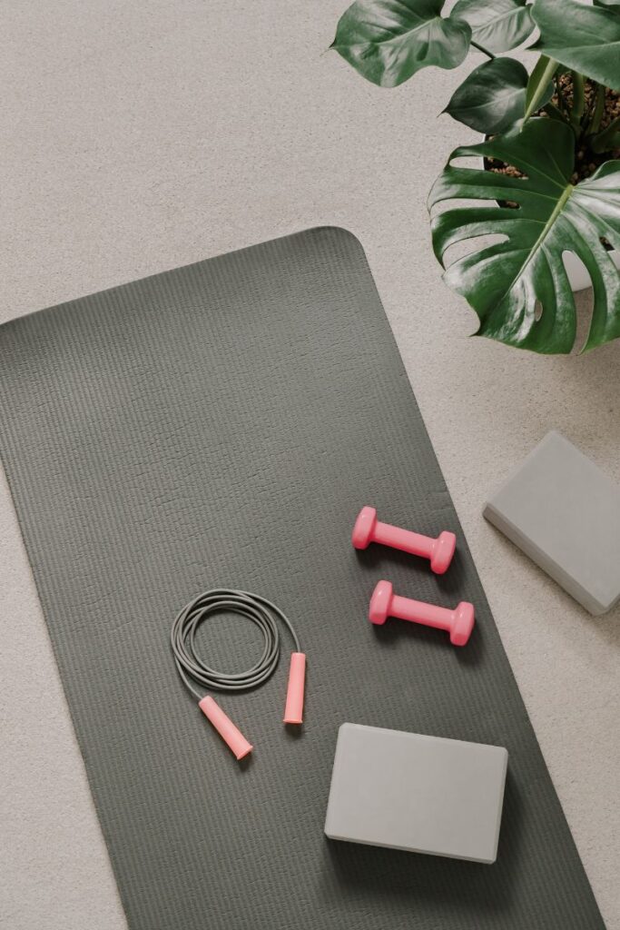 A yoga mat that's been rolled out. Sitting atop it are two dumbbells and a jump rope.