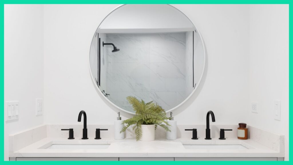 A cleaned bathroom sink, with a round mirror on the wall