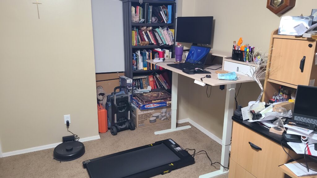 A decluttered corner of an office, with a walking pad and standing desk